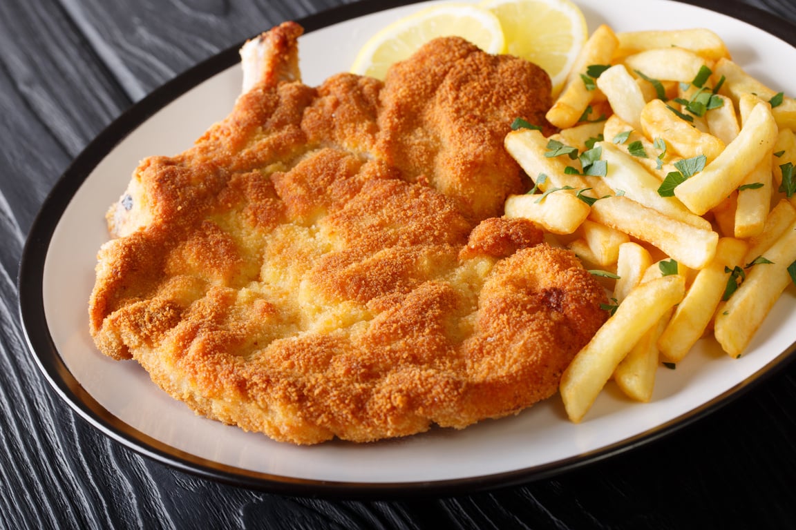 Veal alla Milanese (cotoletta alla milanese) with French fries close-up on a plate. Horizontal